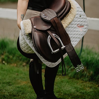 equestrian holding a saddle, saddle blanket and horse accessories