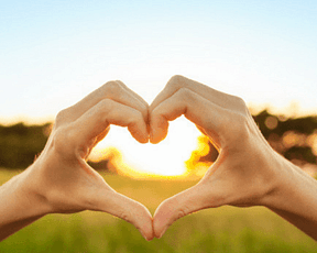 Two hands making a heart with sunshine in background