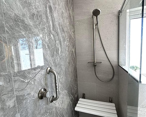 Accessible shower with stylish tiles, built-in seat, and stainless steel grab rail for safety