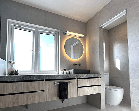 Bathroom renovation featuring a modern vanity with a round mirror light and a separate toilet visible in the background