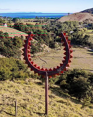 Ra artwork by Chris Charteris overlooking the bush and sea of Kuaotunu on the Coromandel Peninsula