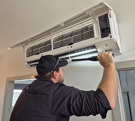 Image of a technician using a light to look inside a heat pump indoor unit behind the louvres. 