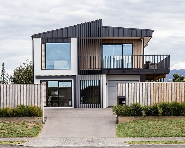The image shows a full home renovation in Papamoa that was completed by local Papamoa Builders. The image shows the newly completed renovation, a modern home with large windows, new joinery, a deck, and cladding. This image shows the best builder's workmanship. 