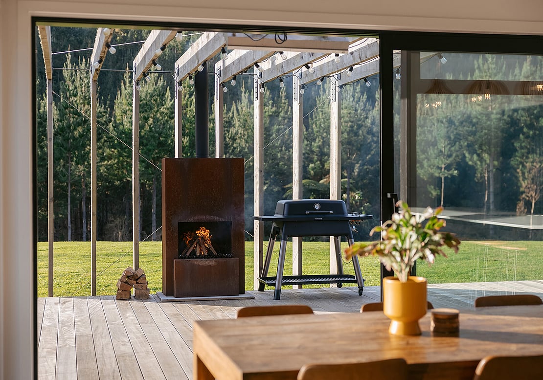 The image shows the view from inside the home out to the new deck, pergola, and outdoor fire.