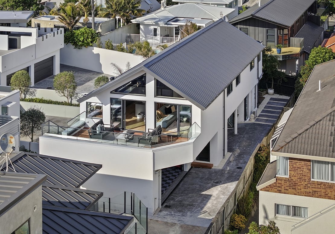The image shows a newly completed renovation by expert renovation builders in Mount Maunganui. The home is modern in style, and the image shows the new roof, cladding, deck, and large windows. 