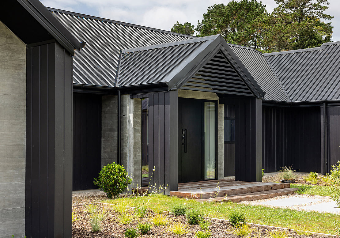 The image shows a new build completed by Straight Up Builders Tauranga, built in rural Katikati. The image shows a mid-shot of the exterior entry, cladding, and roof. 