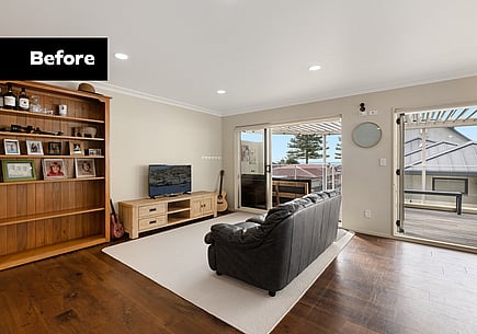 Before image of a dated living space with dark flooring, a couch, and a bookcase, before the home renovation. 