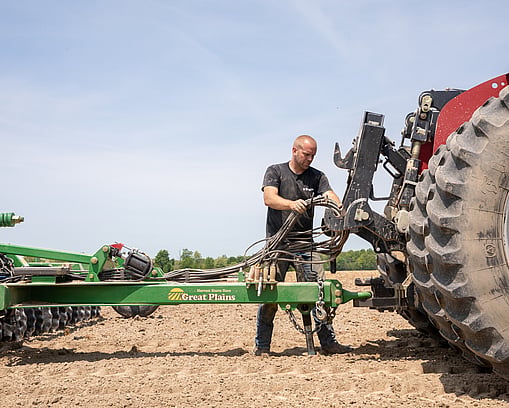 Farmer connecting an implement behind the tractor, hooking up cables