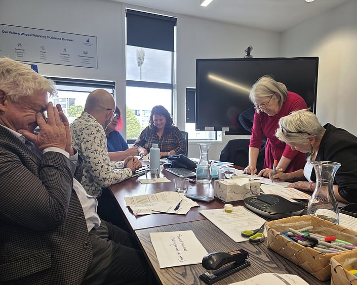 Small group working together at a meeting table, reviewing notes and writing ideas during a strategic planning session.