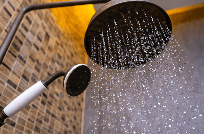 Rainfall shower head running hot water in a tiled bathroom