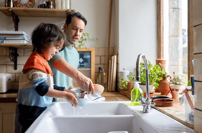 Father and child washing dishes together at a kitchen sink