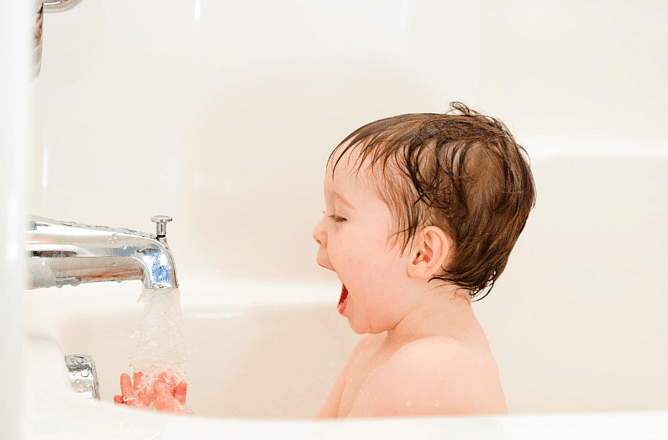 Happy baby in a bath filling with warm water from the tap