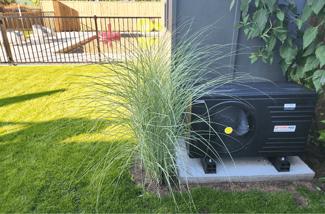 Outdoor hot water heat pump unit installed in a garden beside ornamental grasses