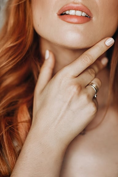 Cropped image of ginger haired woman with hand to face showing engagement and wedding rings.