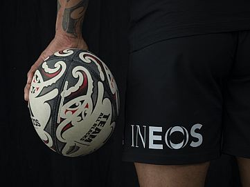 An image of a rugby ball being held next to some shorts with the INEOS logo
