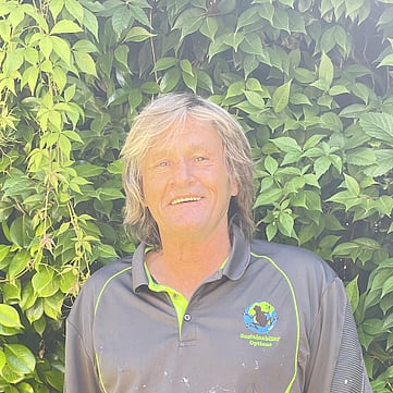 Ian smiling at camera, greenery behind him