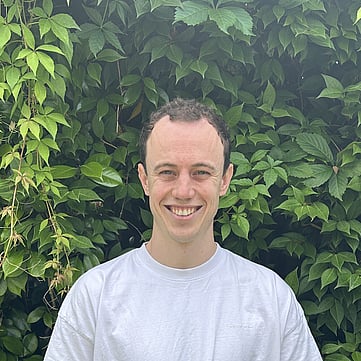 Caleb smiling at camera, greenery behind him