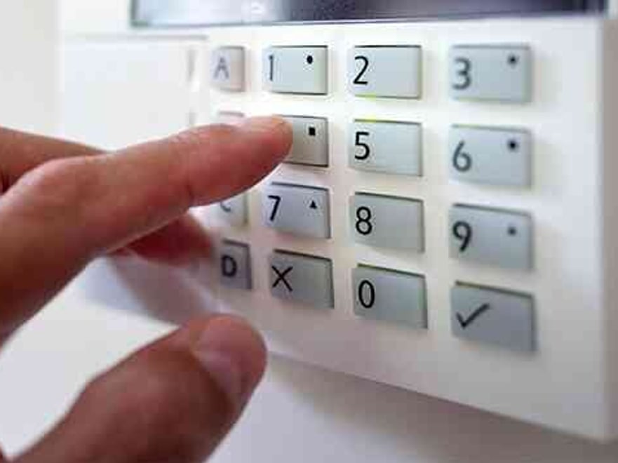 an alarm keypad with a hand in view.