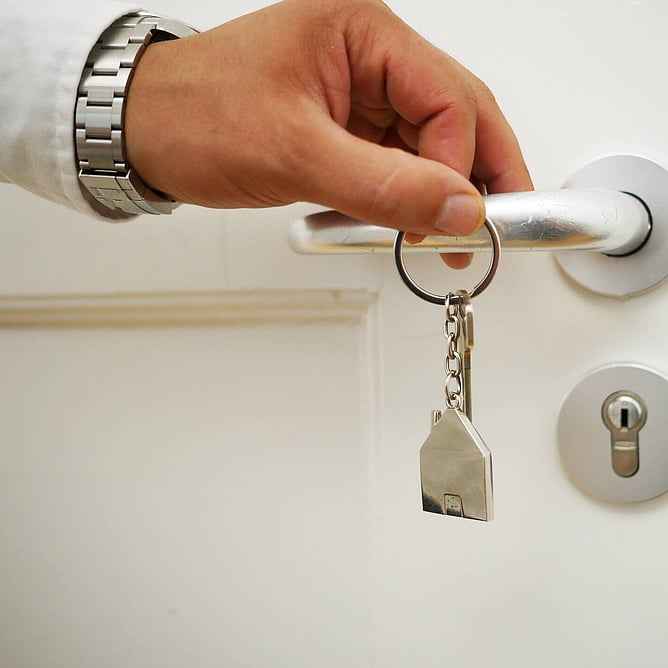 A man's hand holding a house shaped key ring and holing a door handle with a lock below