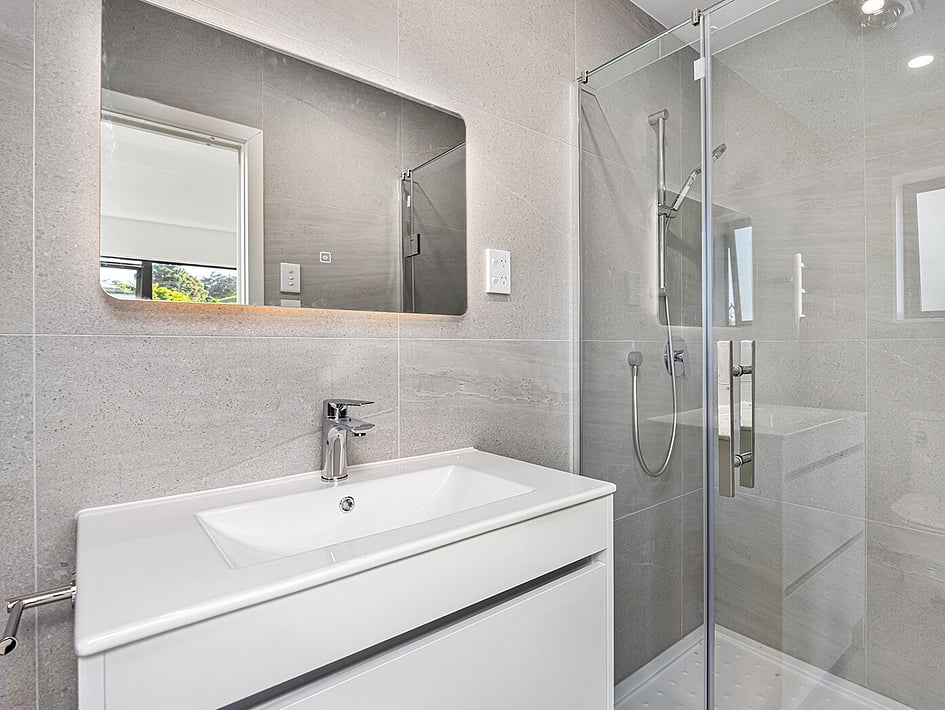 Bathroom with stony coloured tiles and white basin in Eden Construction’s new build house on Mountain Road, Mangere Bridge, Auckland.