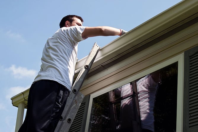 man on ladder checking the gutters