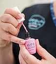 A close up photo of a beauty therapist holding a pale pink OPI Gel colour polish with the lid off and brush out