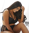 A lady sitting with long dark hair and lovely natural looking spray tan in black crop top and pants