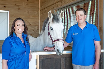 Laura Daly pictured with Scott Munro standing in a Harrison Lane stable with a grey horse
