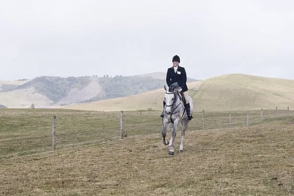 Laura Daly rides a grey horse across a hunt field in Taupo NZ