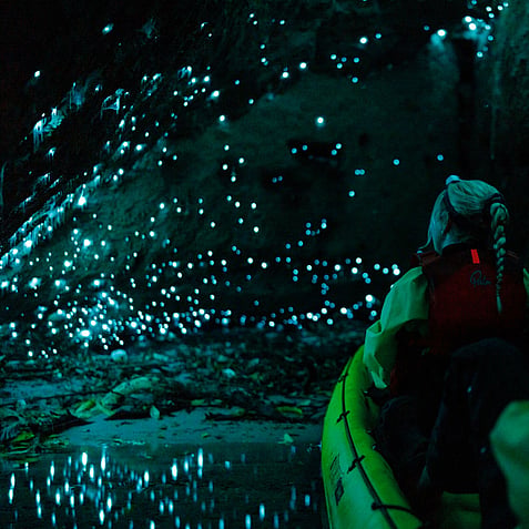Kayak surrounded by glow worms in Rotorua cave, reflections lighting up the water at night