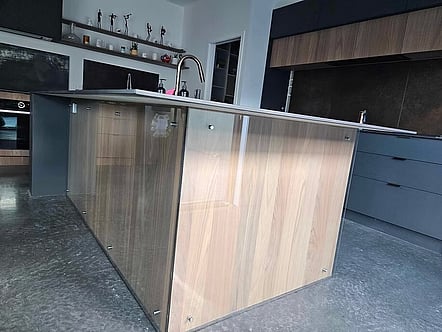 Glass panel on satin standoffs used as a protective barrier from kids feet on the wooden paneling in kitchen island
