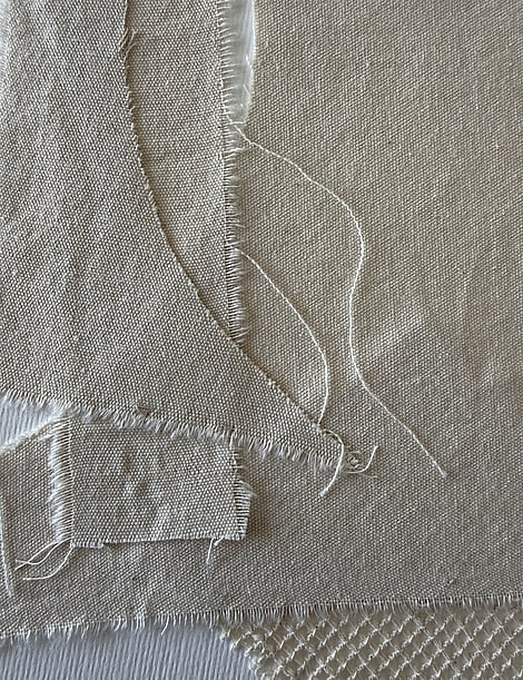 detail image of layered soft honey-toned cotton fragments on ivory fabriano, showing varying weave textures, soft frayed edges and hanging threads 