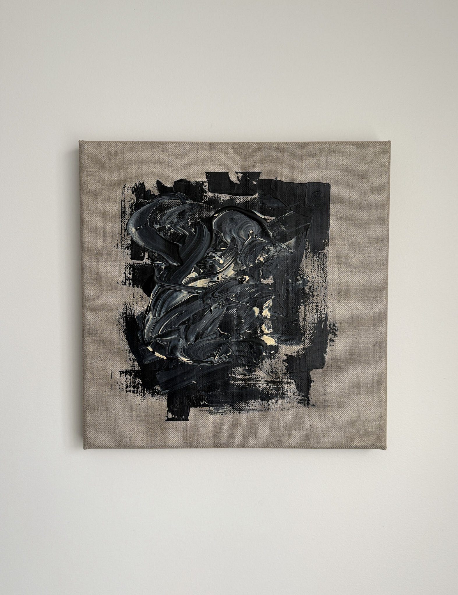 full image showing a black and pale cream textural impasto abstract painting with sweeping curved brushstrokes over a layered black rectangular field, framed by a wide exposed linen border 