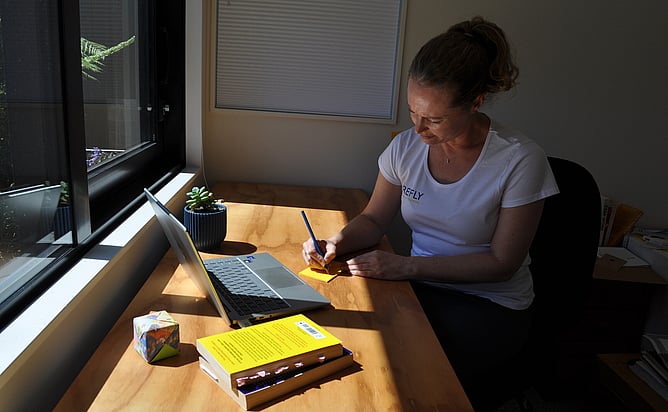 A woman sitting at a desk bathed in sunshine writing a note