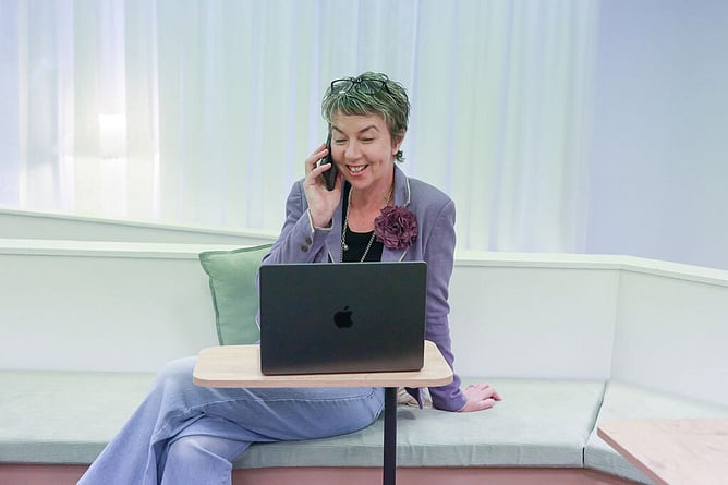 maree gately marketing strategist from spread the word in nz sitting on a corner couch with laptip in front, legs crossed and photo to her ear with glasses on her head