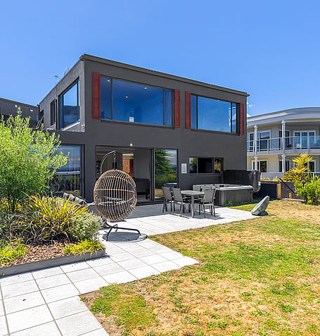 Modern black two-storey holiday home in Taupō with landscaped garden, outdoor seating, and hanging egg chair