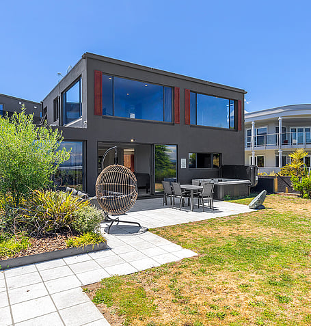 Modern black two-storey holiday home in Taupo with landscaped garden, outdoor seating, and hanging egg chair