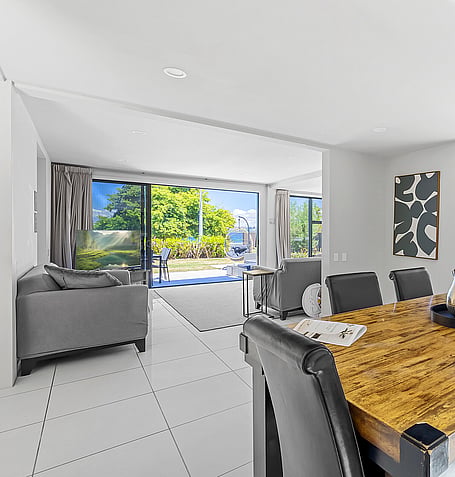 Open-plan lounge with leather seating, wooden dining table, and sliding doors leading to outdoor patio