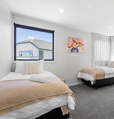 Twin single beds with patterned throws, floral artwork, and street-facing window