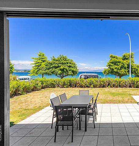 Alfresco dining table on paved patio overlooking lawn and Lake Taupo