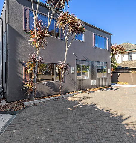 Dark exterior of Gather Taupo with native landscaping and paved driveway