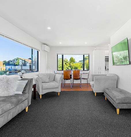 Grey sofas and dining table with chairs, overlooking Lake Taupo through corner windows