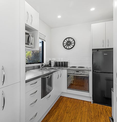 Galley kitchen with white cabinetry, stainless appliances, and timber flooring