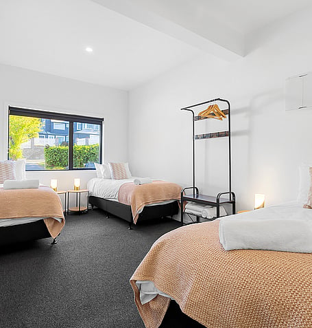 Twin beds with tan throws, dark carpet, and clothing rack in shared bedroom