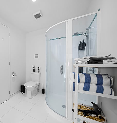 Curved glass shower, white tiling, and shelved towel storage