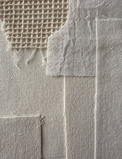 detail of layered neutral toned linens, showing weave, texture and soft frayed edges