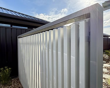 Modern white vertical slat privacy screen beside driveway with planting