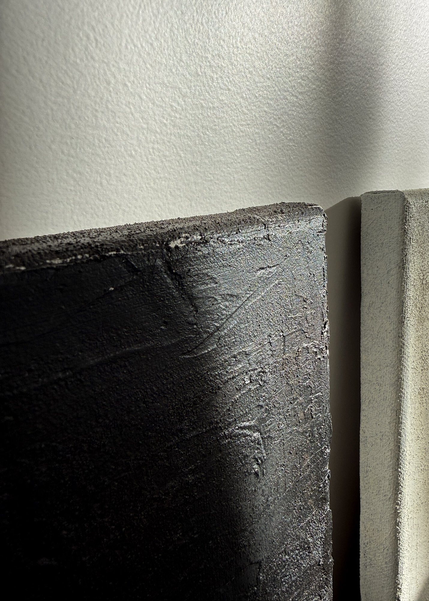 detail image of two textured paintings side by side against a wall with diffused sunlight highlighting mineral surface texture and ridges, painted edges and canvas depth