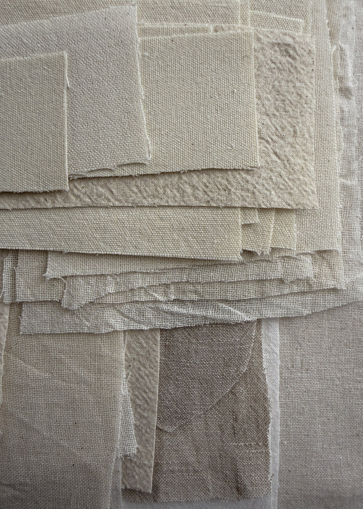 detail image of layered linen and cotton fabrics in a range of oatmeal tones, with overlapping fragments, soft frayed raw edges and varied woven textures creating a tactile surface of soft folds and geometric forms