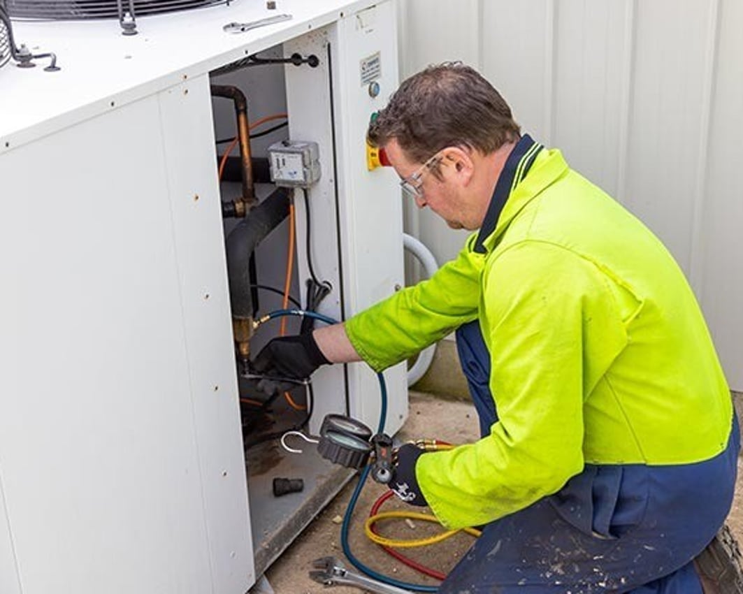 Technician repairing a milk vat refrigeration unit on a dairy farm
